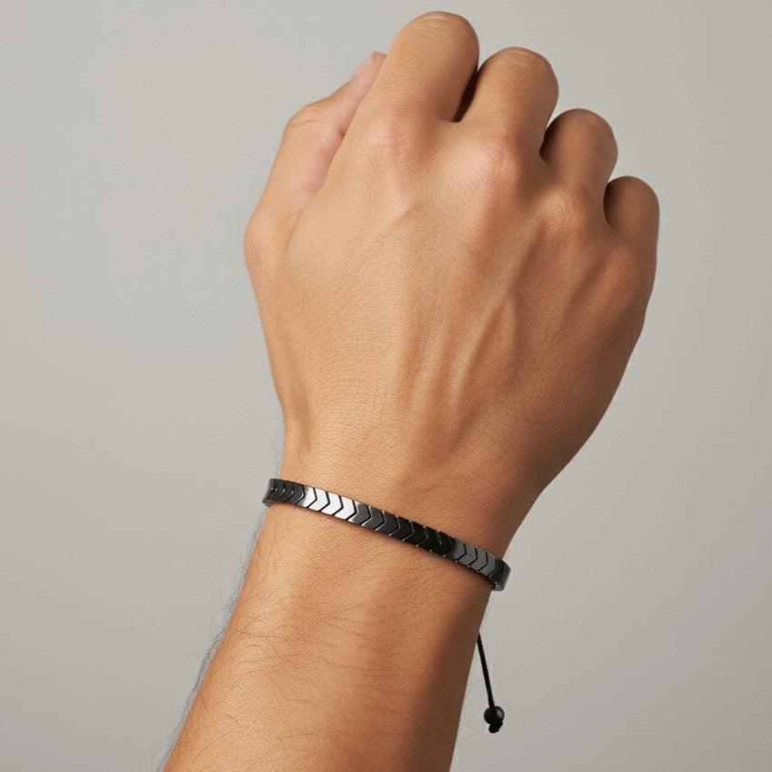 Hand wearing a black and silver bracelet on a gray background