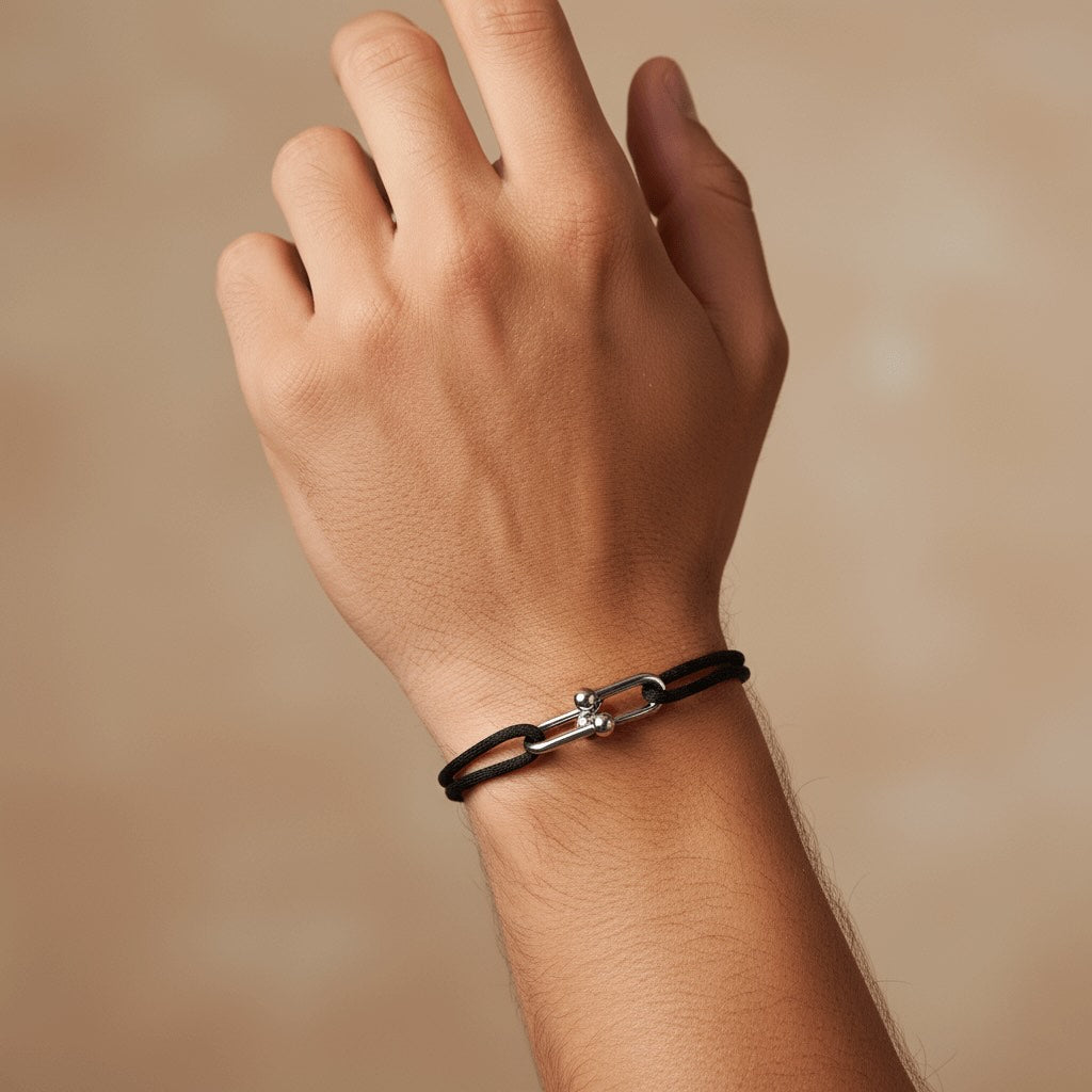 Hand wearing a black leather Velmont bracelet with a silver clasp on a beige background