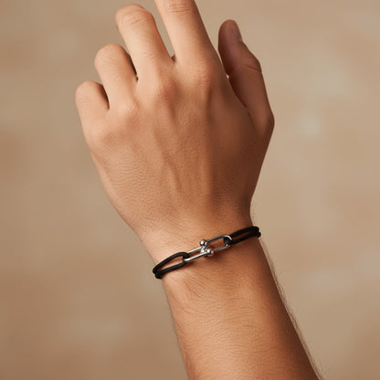 Hand wearing a black leather Velmont bracelet with a silver clasp on a beige background