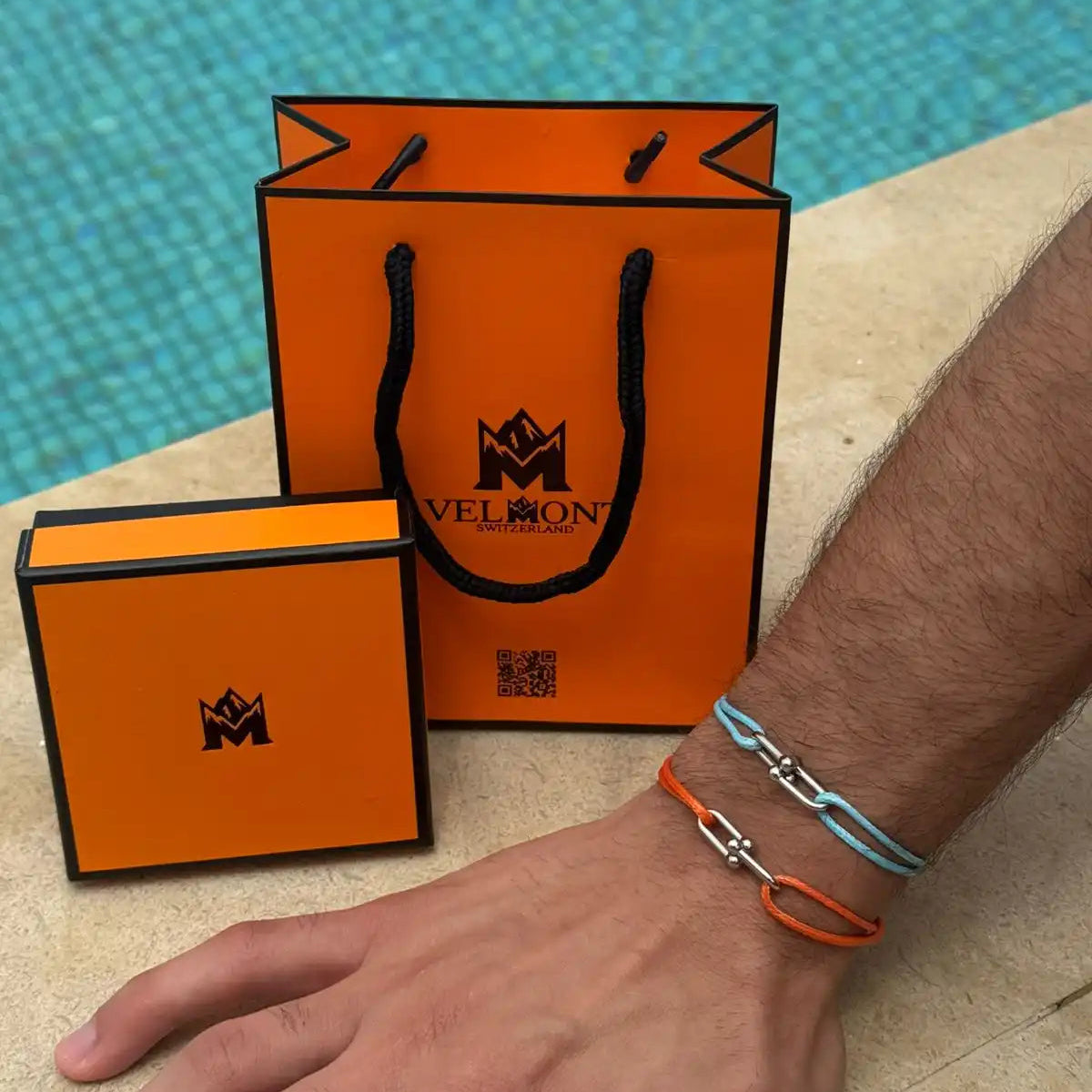 Orange Mellowon shopping bag and box with a hand wearing bracelets by a poolside.