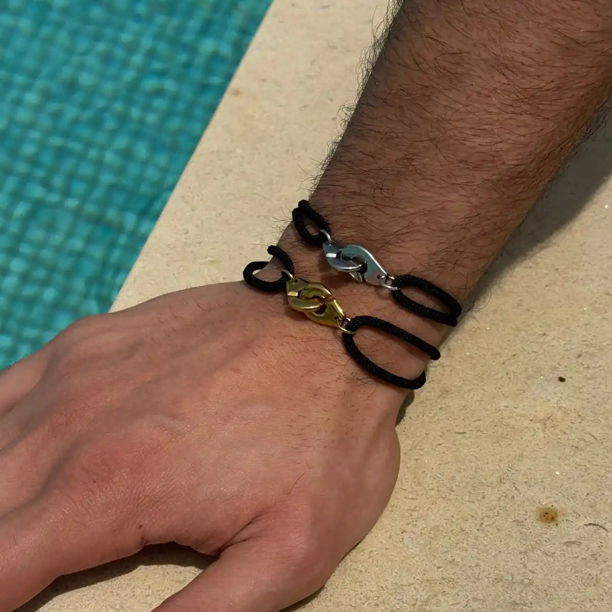 Hand wearing multiple bracelets by a poolside