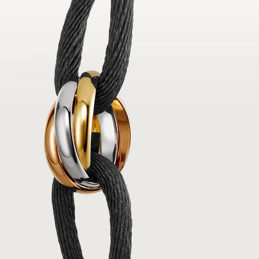 Bracelet with gold, rose gold and silver circular rings on a black cord against a light gray background